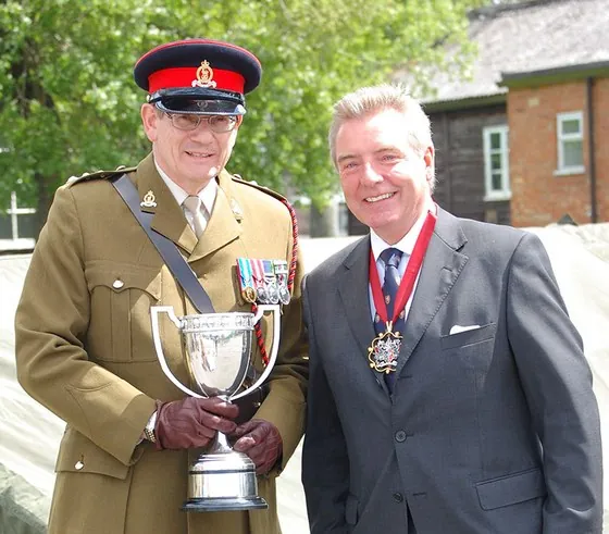 An officer with a silver cup, beside a guest